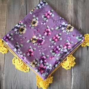 Può includere: Quadrato di tessuto viola con stampa floreale e bordo in crochet giallo.