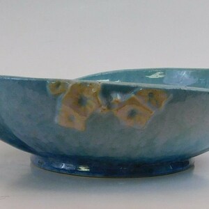 May include: A light blue ceramic bowl with a scalloped edge and a raised design of stylized flowers in shades of yellow and brown.