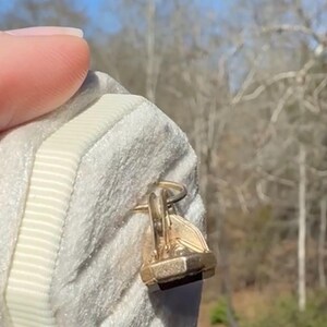 Pu&ograve; includere: Primo piano di un tirazip dorato su un tessuto grigio chiaro strutturato. Il tirazip ha un design geometrico. Un bordo di nastro bianco corre lungo il bordo del tessuto.