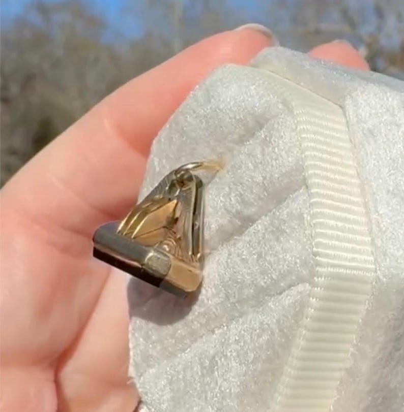 Pu&ograve; includere: Un anello dorato e argentato con un accento rettangolare nero. L'anello &egrave; posto su una superficie bianca e strutturata. Il design dell'anello presenta una forma geometrica con una finitura lucida, che riflette la luce.