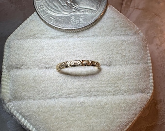 May include: A thin gold band ring featuring an embossed floral pattern along its entire circumference. The ring is positioned next to a United States quarter coin for scale, which measures approximately 0.955 inches in diameter.