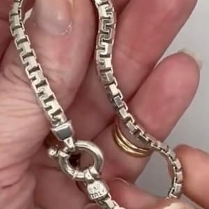 May include: A silver-toned box chain necklace featuring square-shaped links and a circular spring ring clasp. The clasp is stamped with the text 925 ITALY, indicating the metal composition and origin. The chain has a polished, reflective finish.