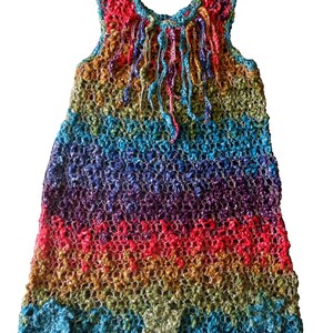 May include: A sleeveless, rainbow-colored crochet dress. The dress features a textured, open weave design with horizontal stripes of red, orange, yellow, green, blue, and purple. The neckline and hem have a scalloped edge, and the top has dangling fringe.
