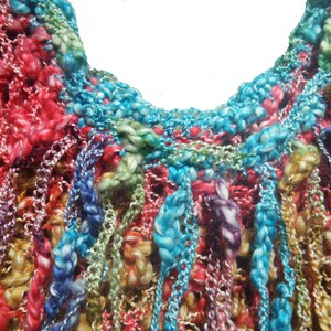 May include: Close-up of a colorful, hand-knitted textile. The piece features a variety of colors including red, blue, green, and yellow. The texture is thick and textured, with a mix of open and closed knit patterns. The overall effect is vibrant and artistic.