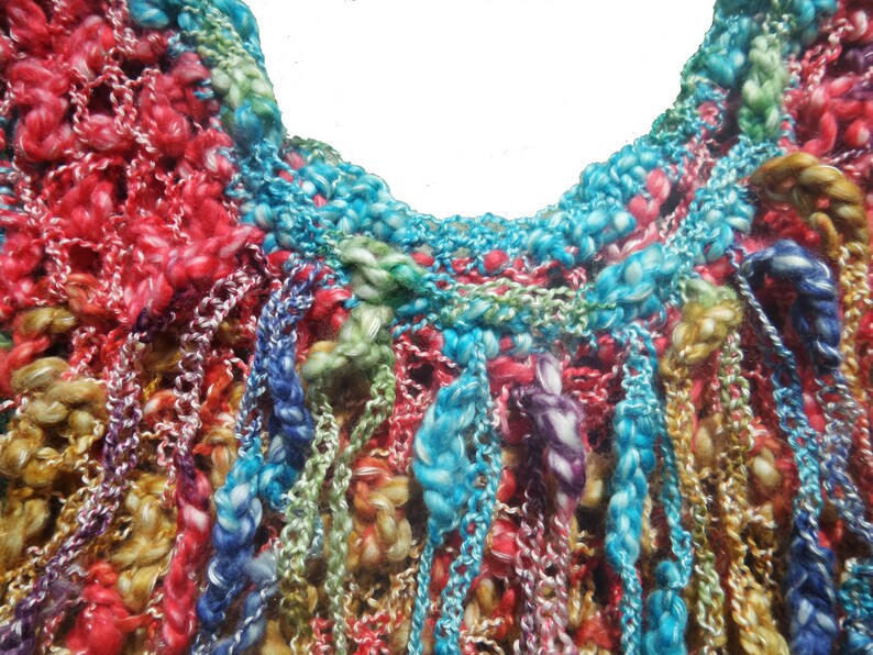 May include: Close-up of a colorful, hand-knitted textile. The piece features a variety of colors including red, blue, green, and yellow. The texture is thick and textured, with a mix of open and closed knit patterns. The overall effect is vibrant and artistic.