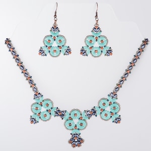 Op de afbeelding: Een turquoise en zilveren kralenketting met bijpassende oorbellen. De ketting heeft een centraal sieraad met een bloemmotief en de oorbellen zijn driehoekig.