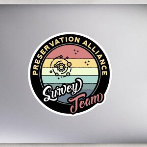 May include: A black and white sticker with a retro design. It features a circle with the text "Preservation Alliance Survey Team" and a stylized image of a solar system with planets and stars.