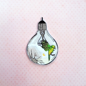 May include: An embroidered patch of a lightbulb with a green and yellow bird inside. The bird is flying upwards and the lightbulb is cracked.