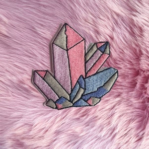 May include: A colourful embroidered patch featuring a cluster of pink, purple and blue crystals. The crystals are arranged in a geometric pattern and have a shiny, iridescent finish.