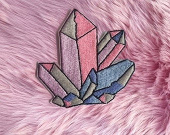 May include: A colorful embroidered patch featuring a cluster of pink, purple, and blue crystals. The crystals are arranged in a geometric pattern and have a shiny, iridescent finish.
