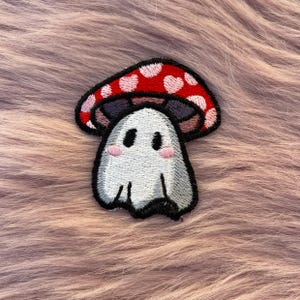 Puede incluir: Parche bordado termoadhesivo con un fantasma blanco que lleva un hongo rojo con corazones rosas.