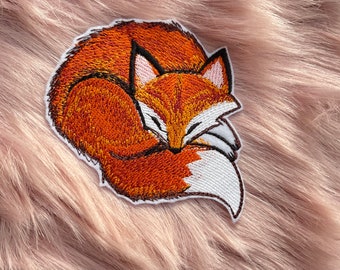 May include: Embroidered patch of a curled up orange fox with white accents, sleeping on a pink fuzzy surface.