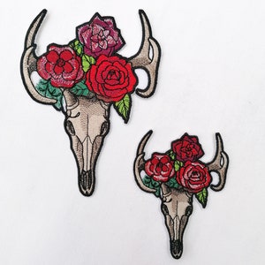 May include: Two embroidered patches featuring a deer skull with red and burgundy roses. The larger patch is approximately 4 inches tall and the smaller patch is approximately 2 inches tall.