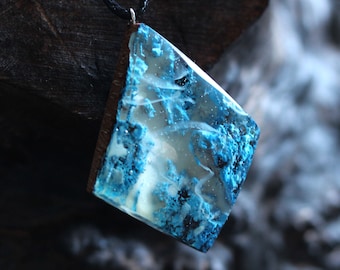 May include: A blue and white resin pendant with a black cord. The pendant has a unique, marbled pattern with white swirls and blue flecks.