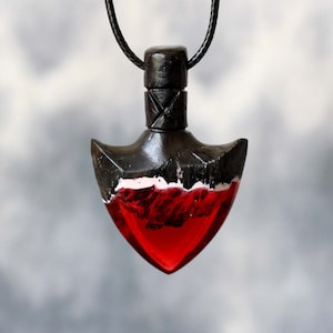 May include: A black wooden pendant with a red resin heart shaped insert. The pendant is on a black cord.
