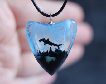 May include: A blue and black heart-shaped pendant necklace with a silhouette of a hammerhead shark inside. The pendant is made of resin and has a black cord.