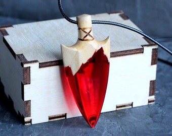 May include: A red and wood arrowhead pendant necklace. The arrowhead is made of wood with a red resin filling. The necklace is on a black cord.