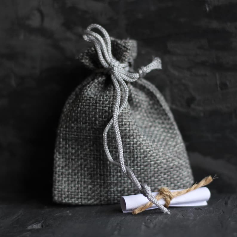 May include: A small gray burlap sack with a white paper note tied to it with twine. The sack is tied with a gray string.