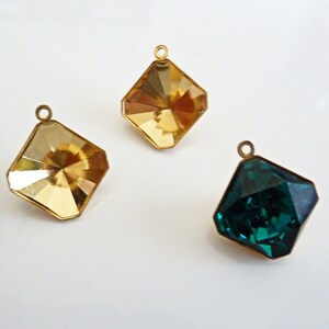 May include: Three gold-toned metal charms with faceted glass stones. Two charms have clear yellow stones and one charm has a dark green stone.