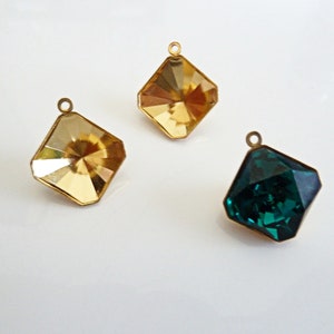 May include: Three gold-toned metal charms with faceted glass inserts. Two charms have clear yellow glass inserts and one charm has a dark green glass insert.
