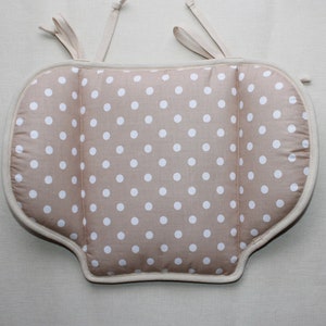 Può includere: Un cuscino per seduta beige con un motivo a pois bianchi. Il cuscino ha una forma sagomata con lati arrotondati e una sezione centrale rettangolare. Include lacci in tessuto beige chiaro sulla parte superiore per fissarlo a una sedia.
