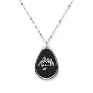 May include: A silver chain necklace with a teardrop-shaped pendant. The pendant features a black background with a colorful mountain scene and a crown with a halo above it.