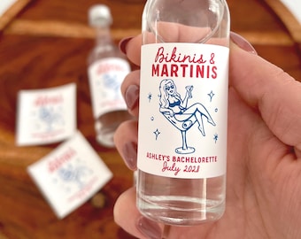 May include: A clear glass miniature bottle with a silver screw cap, featuring a white rectangular label printed with the red text Bikinis & MARTINIS, a blue illustration of a person in a bikini inside a martini glass, and ASHLEY'S BACHELORETTE July 2028.