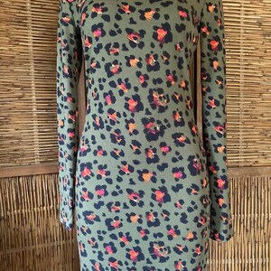 Puede incluir: Vestido de cuello alto verde oliva con estampado de leopardo en negro, naranja y rosa. El vestido de manga larga está hecho de tejido acanalado y tiene un corte ajustado. El vestido se exhibe en un maniquí.