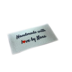 Könnte beinhalten: Weißes Satin-Etikett mit dem Text "Handmade with love by Nana" in schwarzer Schrift und einem kleinen roten Herzen.