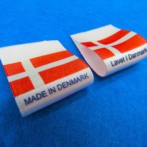 May include: Two white fabric labels with the Danish flag printed on them. One label says "Made in Denmark" and the other says "Lavet i Danmark".