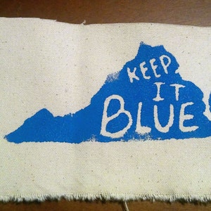 May include: A white canvas patch with a blue outline of the state of Virginia. The words "Keep It Blue" are written in white inside the outline.