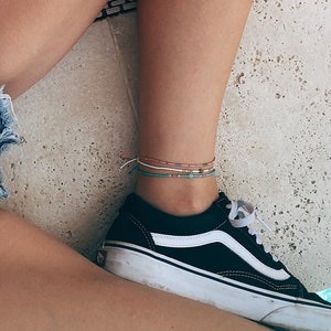 Könnte beinhalten: Eine Person trägt Jeans-Shorts und ein rotes Oberteil, mit einem ausgestreckten Bein und einem schwarz-weißen Sneaker am Fuß. Die Person sitzt am Rande eines Schwimmbeckens.