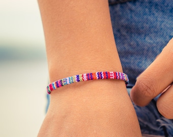 May include: A close-up of a person's wrist wearing a colorful beaded bracelet. The bracelet is made of small, colorful beads that are strung together in a pattern. The bracelet is worn on the left wrist and is visible against the person's skin.