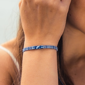 Puede incluir: Una mujer con un top de encaje blanco y una pulsera tejida azul y blanca en la muñeca.