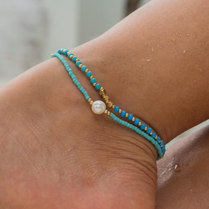 Puede incluir: Dos tobilleras de cuentas turquesa y doradas con un solo dije de perla blanca.