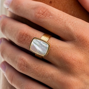 May include: A gold ring with a white mother-of-pearl square stone.
