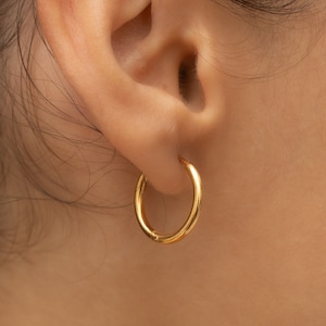 May include: A pair of gold hoop earrings worn in a person's ear.