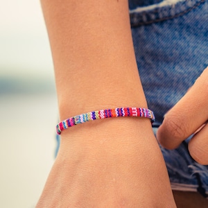 May include: A close-up of a person's wrist wearing a colorful beaded bracelet. The bracelet is made of small, colorful beads that are strung together in a pattern. The bracelet is worn on the left wrist and is visible against the person's skin.