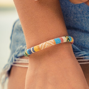 Peut inclure: Un gros plan sur le poignet d'une personne portant un bracelet en perles colorées. Le bracelet est composé de petites perles colorées enfilées les unes aux autres selon un motif. Le bracelet est porté au poignet gauche de la personne et est visible contre la peau de la personne.