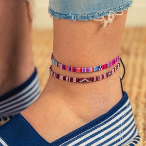 Könnte beinhalten: Ein Paar blau-weiß gestreifte Espadrilles mit einem blauen Band um den Knöchel. Die Person trägt zwei bunte Fußkettchen.