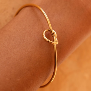 Op de afbeelding: Een gouden armband met een knoopdesign.