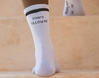 May include: A person wearing white socks with black trim and the text "DON'T FOLLOW ME" on one sock.
