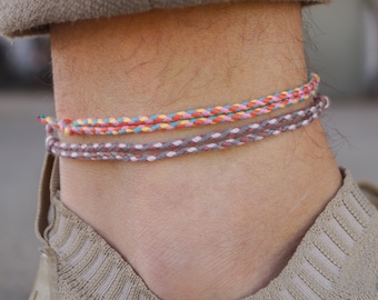 Op de afbeelding: Een beige enkelbandje met drie strengen gekleurde touw.