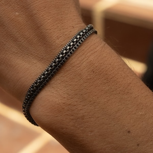 Può includere: Un braccialetto a catena nero con tre file di maglie.