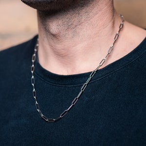 Peut inclure: Gros plan d'une personne portant un t-shirt noir avec un collier en chaîne argentée.