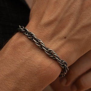 Puede incluir: Un brazalete de cadena de plata con un diseño de cuerda trenzada.