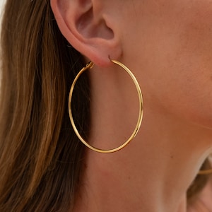 Peut inclure: Boucles d'oreilles créoles en or. Les boucles d'oreilles sont grandes et circulaires, avec une finition lisse et polie.
