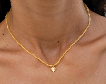 May include: A delicate gold necklace with a small heart pendant. The necklace is made of tiny yellow beads and is perfect for layering.