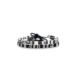 May include: Two black and white woven bracelets with a knot closure.