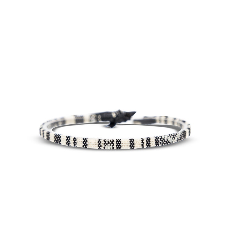 May include: A black and white patterned bracelet made of woven cord.